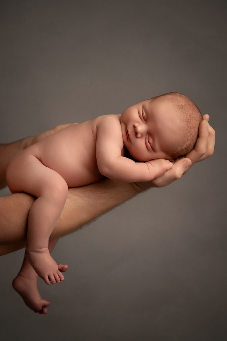 Minimalist newborn photography in Wolverhampton - a peacefully sleeping baby delicately supported by a parent's protective hands.